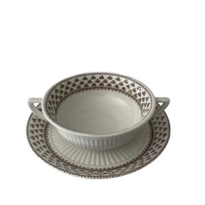 May include: A white porcelain soup bowl with two handles and a matching saucer. Both pieces feature a brown floral pattern.