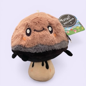 May include: A plush mushroom toy with a smiling face, featuring a brown cap, gray and black accents, and a beige stem. The toy has small arms and a tag that reads "Spirit Exclusive."