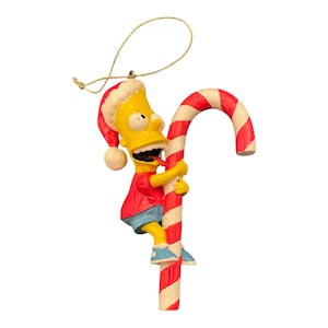 May include: A Christmas tree ornament depicting Bart Simpson from The Simpsons. Bart is dressed in a Santa hat, red top, and blue shorts, holding onto a red and white striped candy cane. A gold string is attached for hanging.