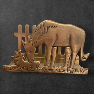 Peut inclure: Une sculpture en métal couleur laiton représentant un cheval et son poulain dans une scène champêtre. Le cheval adulte se tient près d'une petite clôture, tandis que le poulain est couché. La sculpture a un relief détaillé et est montée sur une base rectangulaire.
