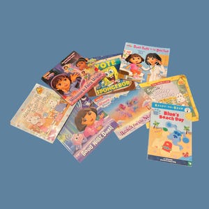 Puede incluir: Una colección de ocho libros infantiles con varios personajes animados. Los títulos incluyen Dora la Exploradora: Bienvenida al Mundo de las Hadas, Dora va al Doctor, ¡Buenas noches, Dora!, La sorpresa de Pascua de Max, Sunny Bunny Tales y Blue's Beach Day.
