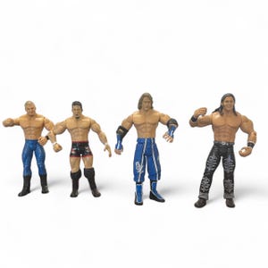 May include: Four action figures of muscular men in wrestling attire. The figures are in various poses, with detailed facial features and painted clothing. The figures are on a white background.