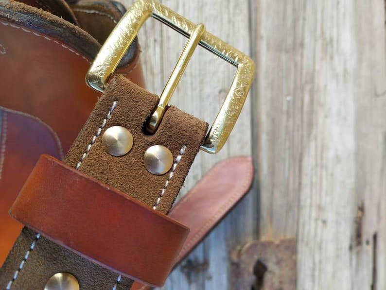 May include: Close-up of a brown leather belt with a brass buckle. The belt has a brown suede lining and two silver rivets.