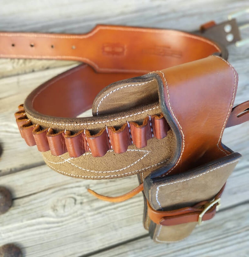 May include: A brown leather gun belt with a holster and a suede lining. The belt has a row of loops for bullets.