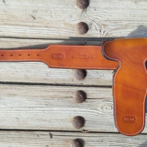 May include: A brown leather gun belt with a holster. The belt has a white stitching detail and the text "Bill-Man" is embossed on the belt and holster.