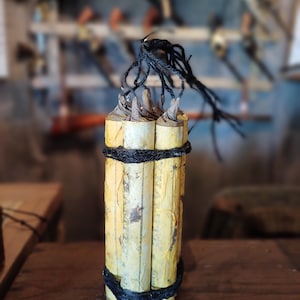 Può includere: Un fascio di quattro tubi di carta gialla legati insieme con uno spago nero. I tubi sono avvolti in carta marrone e hanno una consistenza ruvida.