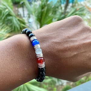 May include: Black beaded bracelet with red, white, and blue accents. The bracelet features a silver charm with a floral design.