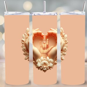 Könnte beinhalten: Ein pfirsichfarbener Edelstahlbecher mit einem Design aus zwei Händen, die ein Herz mit einem kleinen Herzen und dem Zeichen für 'Ich liebe dich' in Deutscher Gebärdensprache in der Mitte bilden. Das Design ist von einem floralen Kranz umgeben.