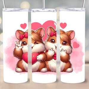 Könnte beinhalten: Zwei braune Hamster halten rosa Herzen mit rosa Herzen und einem rosa Aquarellhintergrund auf einem weißen Becher.