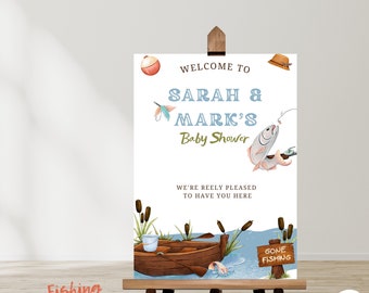 Op de afbeelding: Een welkomstbord voor een babyshower met een vissersthema. Het bord is wit met blauwe en groene accenten. Het staat "Welcome to Sarah & Mark's Baby Shower" en "We're Reely Pleased to Have You Here". Er is een cartoonafbeelding van een boot met een hengel en een vis die uit het water springt. Het bord heeft ook een bord met de tekst "Gone Fishing".