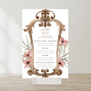 Könnte beinhalten: Ein druckbares Schild mit einem dekorativen Rahmen und floralen Akzenten. Das Schild listet Signature-Getränke für eine Party auf, darunter Wein, Bier und alkoholfreie Optionen. Der Text lautet "A little BOO is almost due."