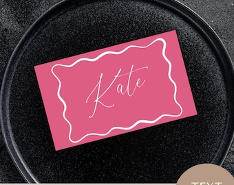 May include: A blush pink place card with a white wavy border and the name "Kate" in elegant script. The card is on a black plate. The text "BLUSH PLACE CARD" and "2.5x1.5" WAVE FRAME TEMPLATE" are at the bottom.