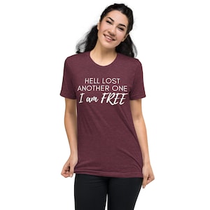 May include: A maroon heather t-shirt with the text "Hell lost another one I am FREE" in white.
