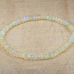 Può includere: Un delicato braccialetto composto da piccole perle di opale iridescenti. Le perle sono di colore bianco latte con lampi di tonalità arcobaleno. Il braccialetto è infilato insieme, formando una forma circolare. Le perle di opale sono rotonde e lisce.