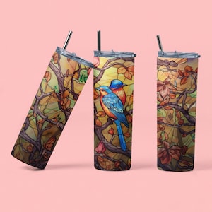 Op de afbeelding: Drie roestvrijstalen bekers met een glas-in-loodontwerp met twee blauwe vogels die op een tak zitten met gele, oranje en bruine bladeren.