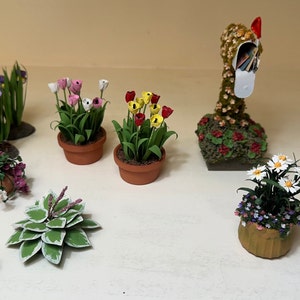 May include: A collection of miniature potted plants with various flowers, including tulips, daisies, and irises. The plants are arranged on a white surface, with a miniature mailbox in the background.