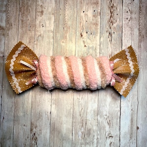 Puede incluir: Un calcetín de Navidad en forma de bastón de caramelo rosa y marrón con purpurina dorada y una cinta blanca y rosa.