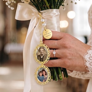 May include: A wedding bouquet charm featuring two oval gold-toned filigree frames containing photographs of people, attached to a gold chain with white pearls and a round gold disc engraved with the text, you are always in my heart.
