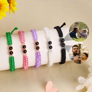 May include: Five colourful friendship bracelets with black beads. The bracelets are made of woven string and are tied with a knot. The bracelets are displayed on a white surface.