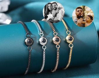 May include: Four silver bracelets with a small round charm that projects an image when viewed through a small hole. The charms are black, silver, gold, and rose gold.