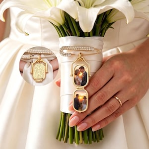 May include: A gold-toned metal brooch pin featuring a row of clear crystals and a dangling, double-sided rectangular locket. The locket displays two separate photographs of a couple in an outdoor setting. The reverse side of the locket has an ornate, engraved floral pattern.