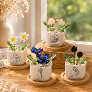 May include: Four square white ceramic planters on round wooden bases, each containing glass flowers and small pebbles. The planters feature custom black line-art illustrations of people and text, including phrases like Our Love Grows Still and To My Soulmate.
