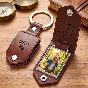 May include: Two brown leather keychains with silver metal rings. One is closed, engraved with DAD and baby footprints. The other is open, revealing a photo of a man and child, with the text I need to say I love you Safe home and a heart.