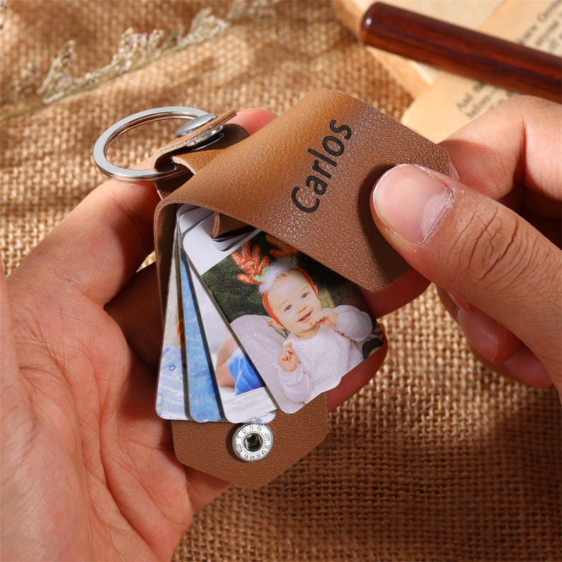 May include: A brown leather keychain with a silver ring and a snap closure. The keychain holds several small photo cards. The word "Carlos" is printed on the leather. The photos show a baby.