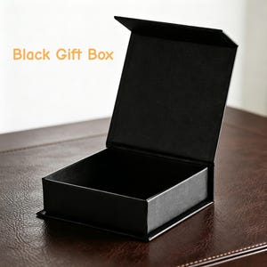 May include: A black gift box with an open lid. The box is rectangular and sits on a brown surface. The text "Black Gift Box" is in the upper left corner.