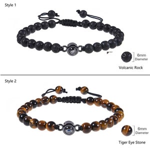 May include: Two styles of beaded bracelets with a black metal charm featuring an evil eye design. The first bracelet is made with black volcanic rock beads and the second bracelet is made with tiger eye beads. Both bracelets have a black cord with a sliding knot for adjusting the size.
