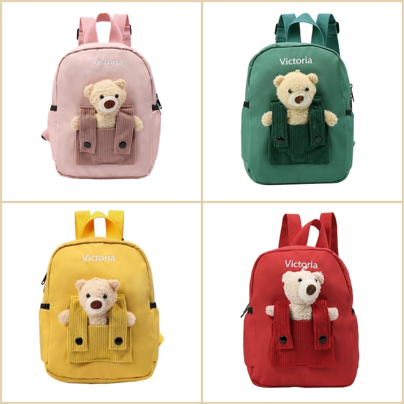 May include: A collection of four small backpacks in pink, green, yellow, and red. Each bag features the name Victoria embroidered in white, adjustable straps, and a plush teddy bear tucked into a corduroy front pocket with two black buttons.