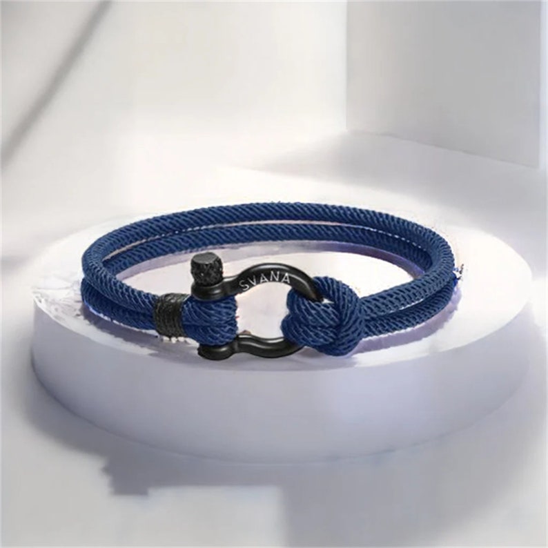 May include: A navy blue rope bracelet with a black metal clasp. The clasp has the word "SVANA" engraved on it.