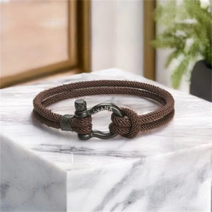 May include: A brown rope bracelet with a black metal clasp. The clasp has the word "SVANA" engraved on it.