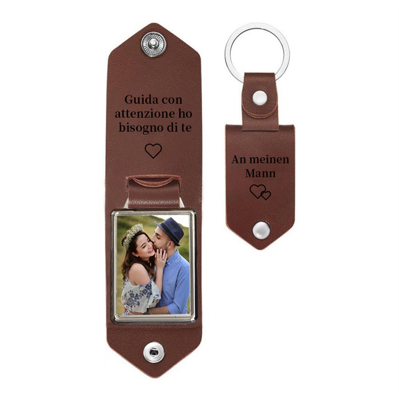 May include: A brown leather keychain and photo holder set. The photo holder has a picture of a couple and the text "Guida con attenzione ho bisogno di te" with a heart symbol. The keychain has the text "An meinen Mann" and two hearts.