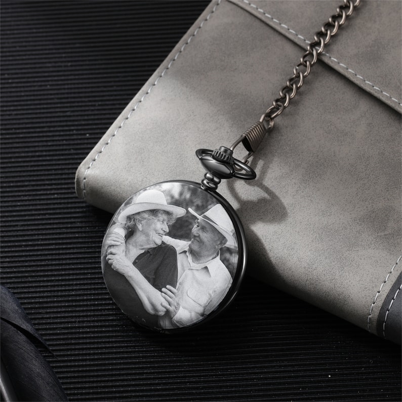 Op de afbeelding: Zwart zakhorloge met een foto van een ouder koppel in zwart-wit. Het horloge heeft een ketting.