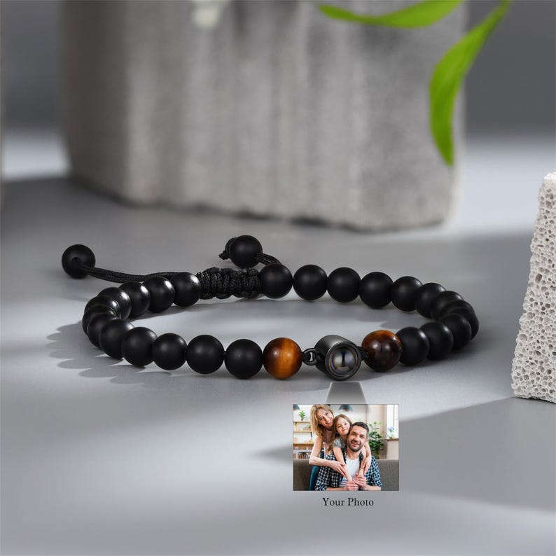 May include: Black beaded bracelet with a small photo insert. The photo insert shows a family of three. The bracelet has a brown tiger eye bead.