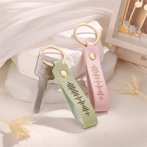 May include: Two leather keyrings with gold rings and a silver key. The keyrings are pink and green with a gold button and a decorative pattern.