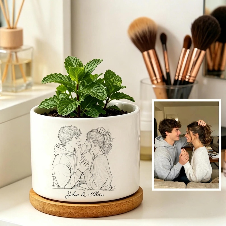 Puede incluir: Una maceta de cer&aacute;mica blanca con una ilustraci&oacute;n en blanco y negro de una pareja, con los nombres "John & Alice" debajo. La maceta contiene una planta verde y descansa sobre un posavasos redondo de madera. Se ve una foto enmarcada de la pareja.