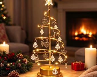 May include: A gold-toned spiral Christmas tree decoration with an illuminated star topper. The structure features integrated warm LED lights and hangs clear, diamond-shaped ornaments and heart-shaped charms engraved with the names Isla, Leo, Rose, and Grace.