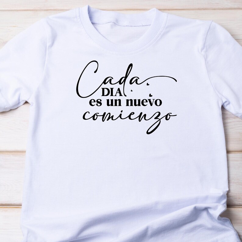 May include: White t-shirt with black text that reads "Cada DIA es un nuevo comienzo" which translates to "Every DAY is a new beginning".