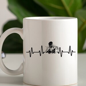 Puede incluir: Taza de cer&aacute;mica blanca con una silueta negra de un soldador con una m&aacute;scara de soldar y una l&iacute;nea de latido del coraz&oacute;n. El texto "My heart beats for welding" no es visible en la imagen.