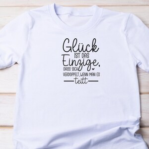 May include: White t-shirt with black text that reads "Gl&uuml;ck ist das Einzige, dass sich verdoppelt, wenn man es teilt" which translates to "Happiness is the only thing that doubles when you share it".