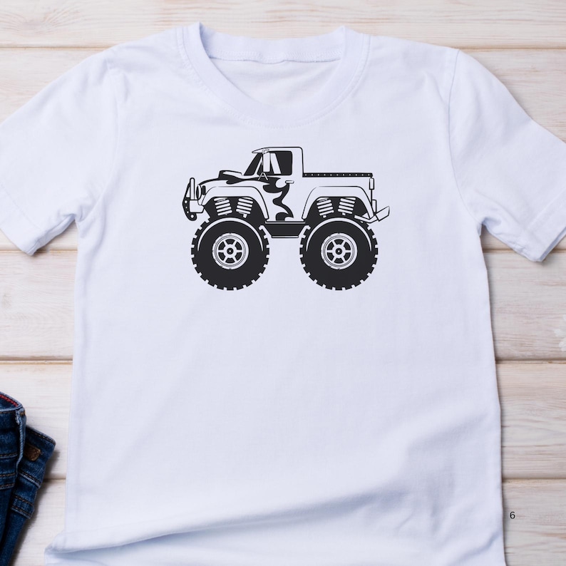 May include: White t-shirt with a black silhouette of a monster truck. The truck has large tires and a pickup bed.