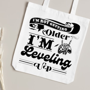 May include: White tote bag with a black graphic that says "I'm not getting older I'm leveling up" with a video game controller graphic.