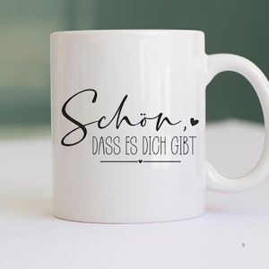 May include: White ceramic mug with black text that reads "Sch&ouml;n, dass es dich gibt" which translates to "It's nice that you exist".