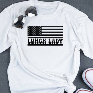 May include: White t-shirt with a black and white American flag graphic and the text "Lunch Lady" in a retro font.