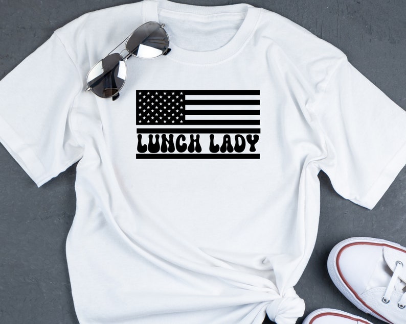 May include: White t-shirt with a black and white American flag graphic and the text "Lunch Lady" in a retro font.