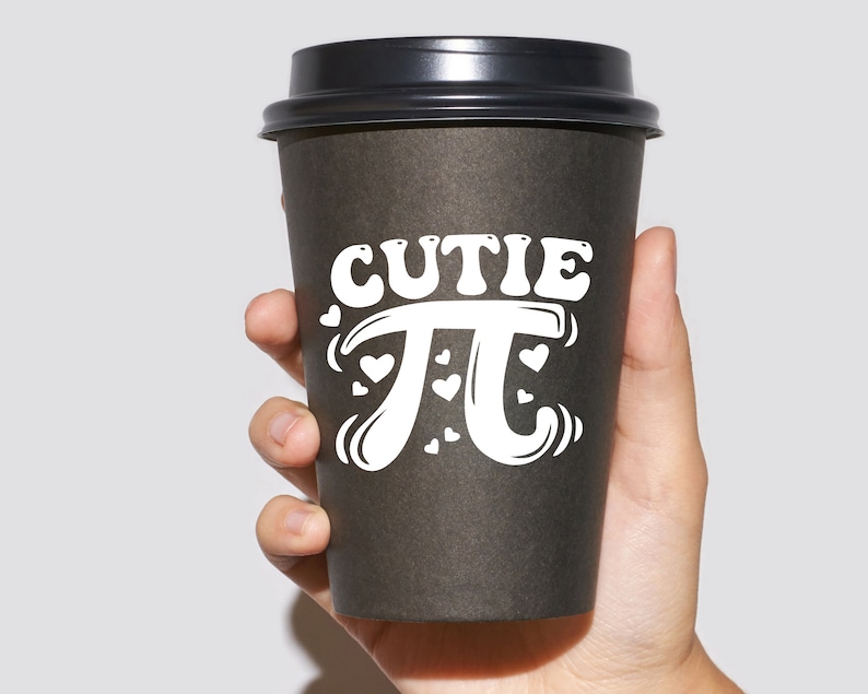 Puede incluir: Un vaso de caf&eacute; para llevar de color negro con un dise&ntilde;o blanco que dice "cutie pi" con corazones alrededor del s&iacute;mbolo pi.