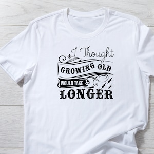 May include: White t-shirt with a black graphic that says "I Thought Growing Old Would Take Longer".