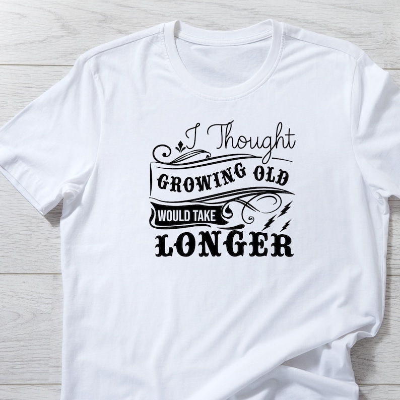May include: White t-shirt with a black graphic that says "I Thought Growing Old Would Take Longer".